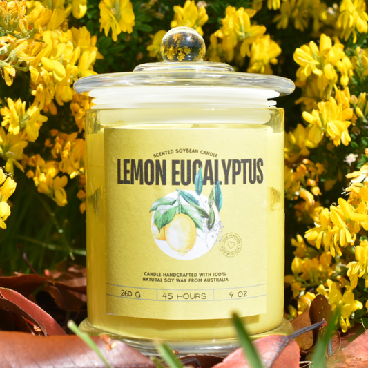 Lemon Eucalyptus candle in a glass jar with a label, surrounded by yellow flowers.